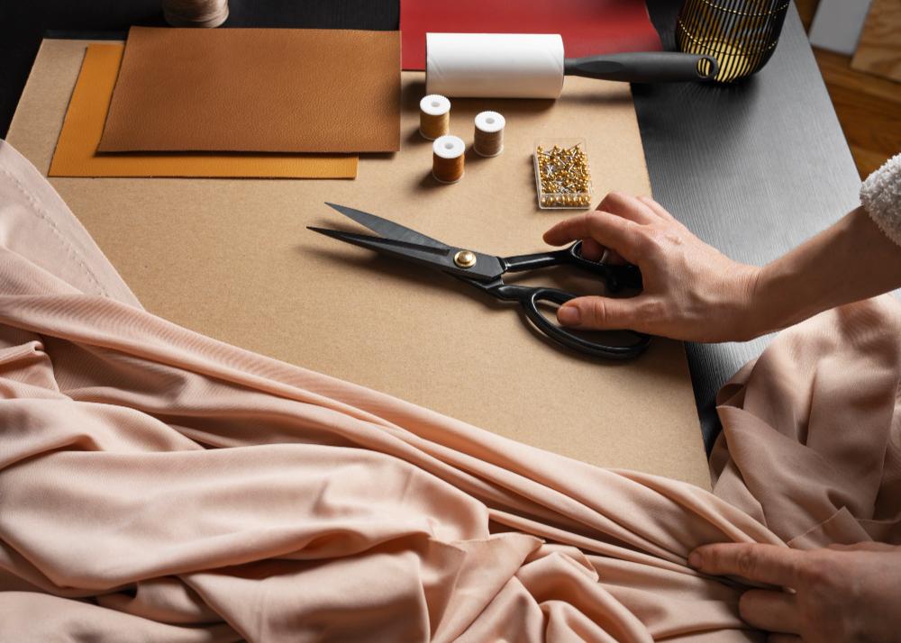 Hand placing fabric scissors on a cutting table beside draped fabric