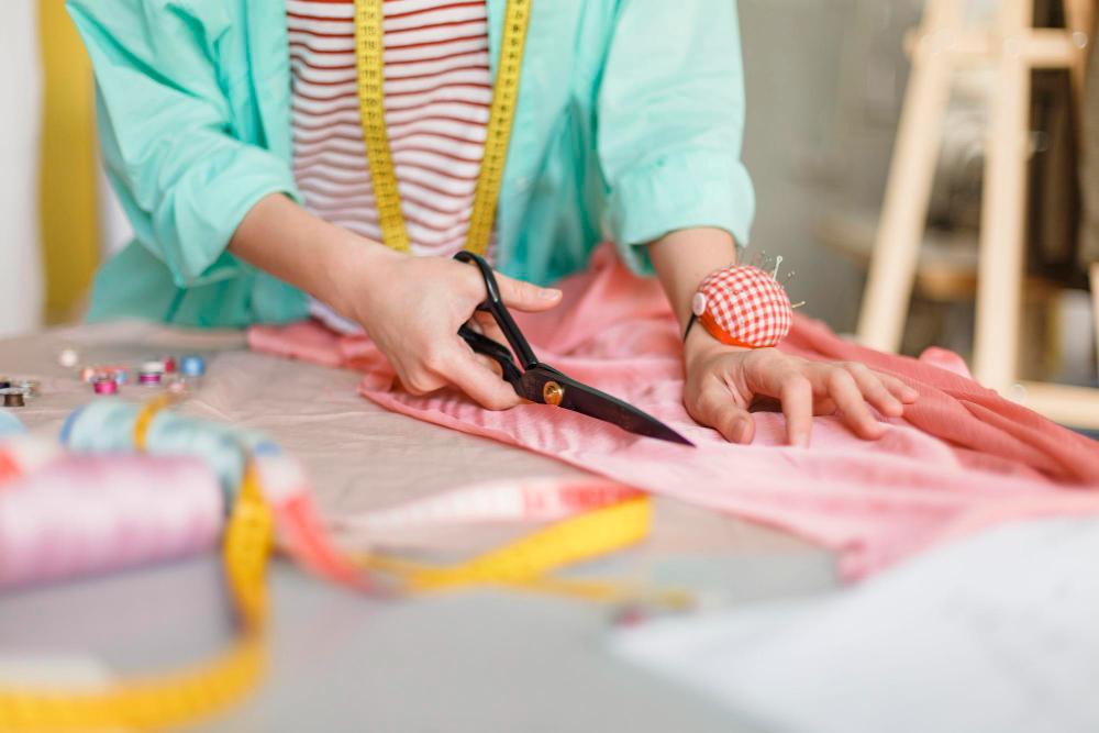 Hands cutting pink fabric with scissors beside a tape measure and thread